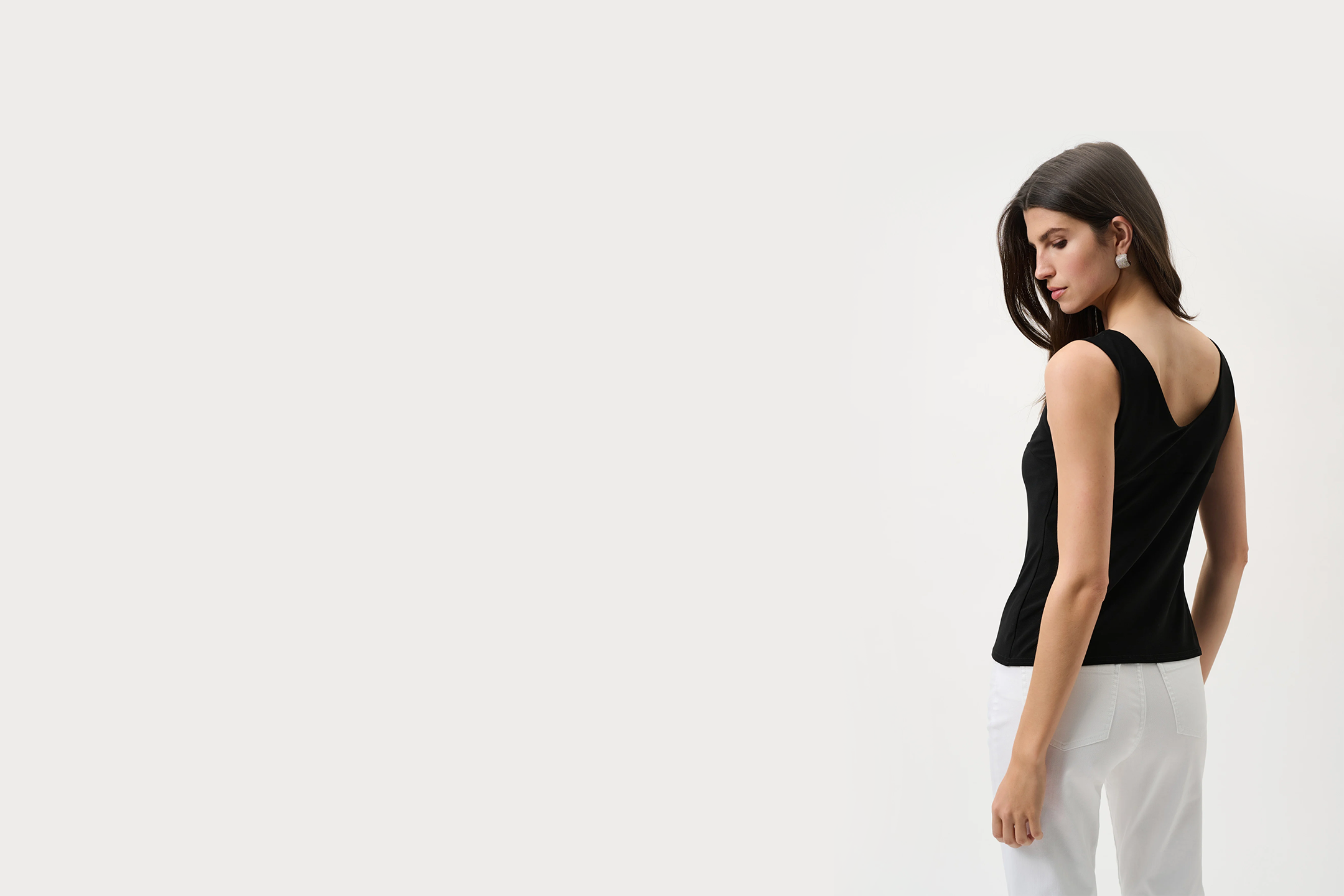 Woman wearing a black sleeveless top and white pants on a light gray background